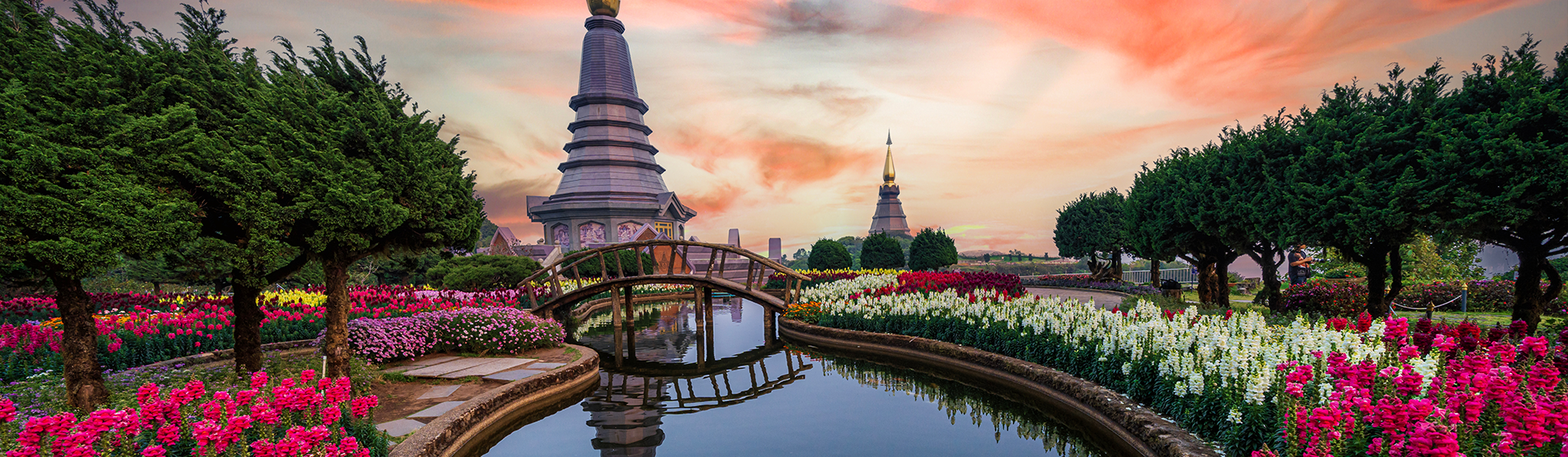 Pagoda set among a garden with colourful blooms and a wooden bridge across a small river in Chiang Mai, Thailand