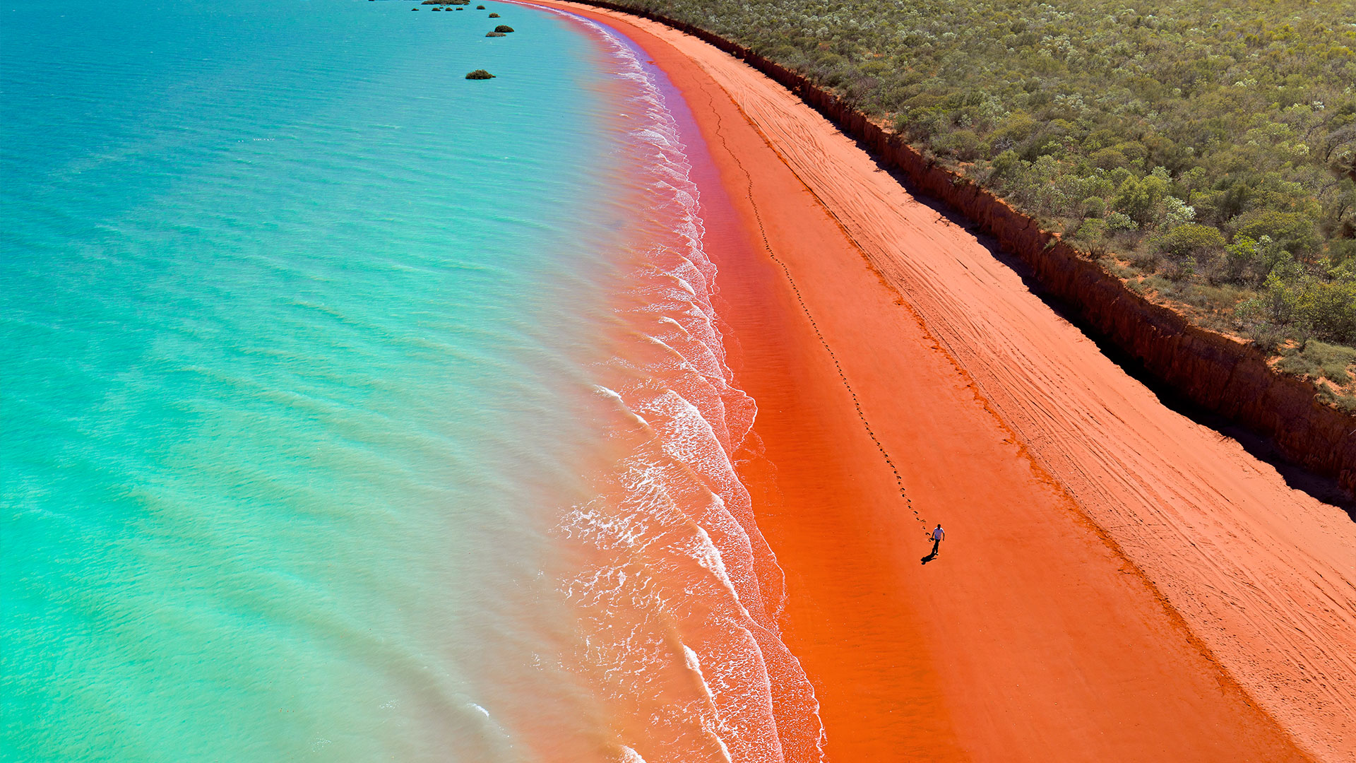 A guy walking along the red sand beach at Roebuck Bay, Western Australia